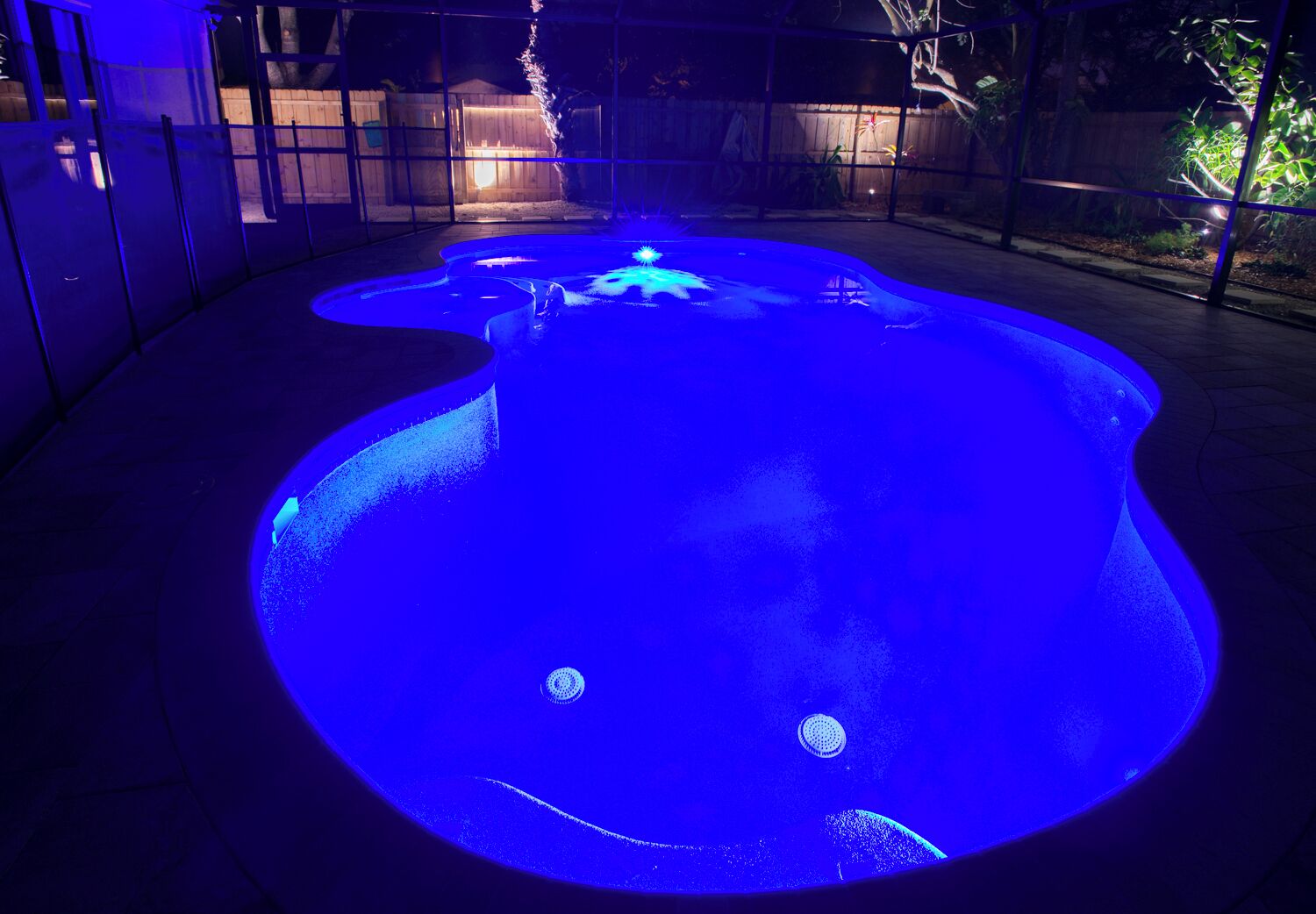 A swimming pool with a unique shape and illuminated by blue lighting.