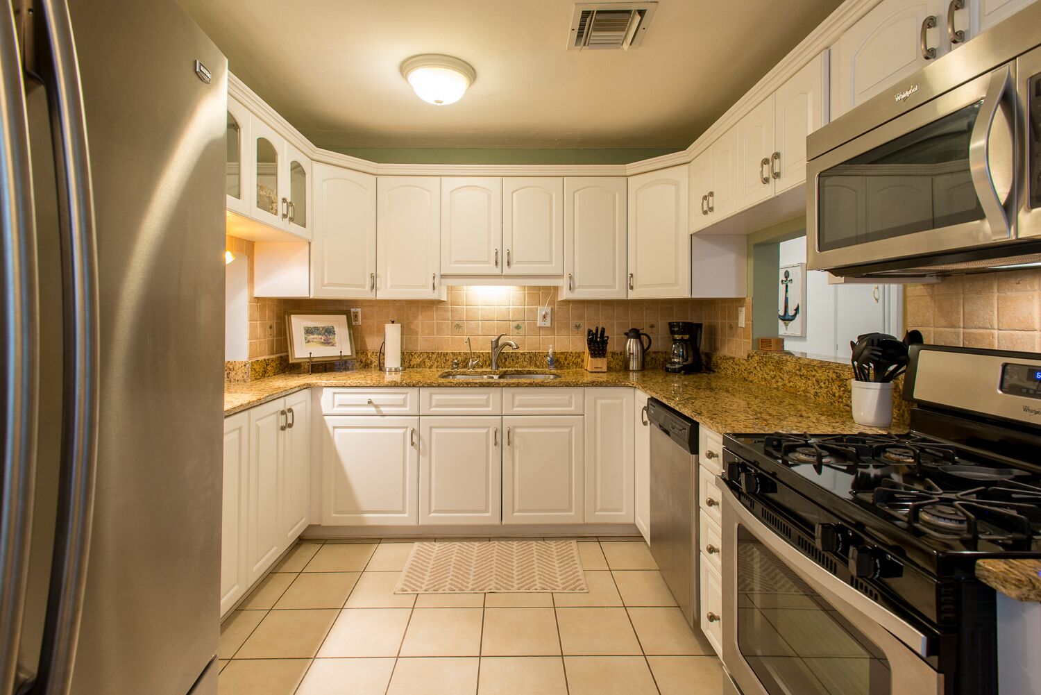 Una cocina con armarios blancos, encimera de granito, refrigerador de acero inoxidable, estufa y microondas.
