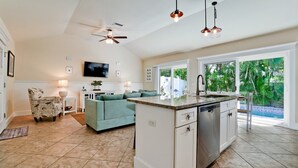 A spacious kitchen with a central island, a dining area with a sofa, and a TV mounted on the wall. - Beach Days, Poolside Nights & Island Memories (Holmes Beach)