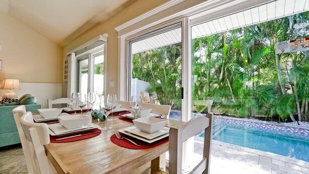 A dining area with a view of a pool and tropical vegetation. - Beach Days, Poolside Nights & Island Memories (Holmes Beach)