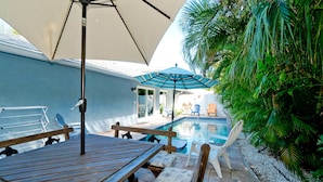 A poolside area with a wooden table, chairs, and umbrellas. - Beach Days, Poolside Nights & Island Memories (Holmes Beach)