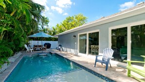A swimming pool with a tiled edge, surrounded by a patio area with chairs and a table. - Beach Days, Poolside Nights & Island Memories (Holmes Beach)