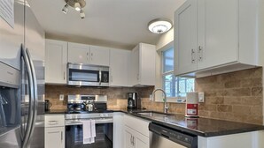 Een moderne keuken met roestvrijstalen apparatuur, witte keukenkastjes en een accentmuur van baksteen.