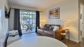 Et hotelværelse med en stor seng, en sofa, et tv ophængt på væggen, et bord med en lampe og udsigt til uderummet gennem store vinduer.