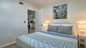 Una camera da letto con un letto, comodini, una lampada da comodino, un quadro e vista sulla cucina.