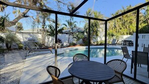 Et overdækket udendørsområde med pool, liggestole og et bord.