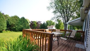 Une terrasse en bois, agrémentée de mobilier d’extérieur, entourée d’un jardin et d’arbres.
