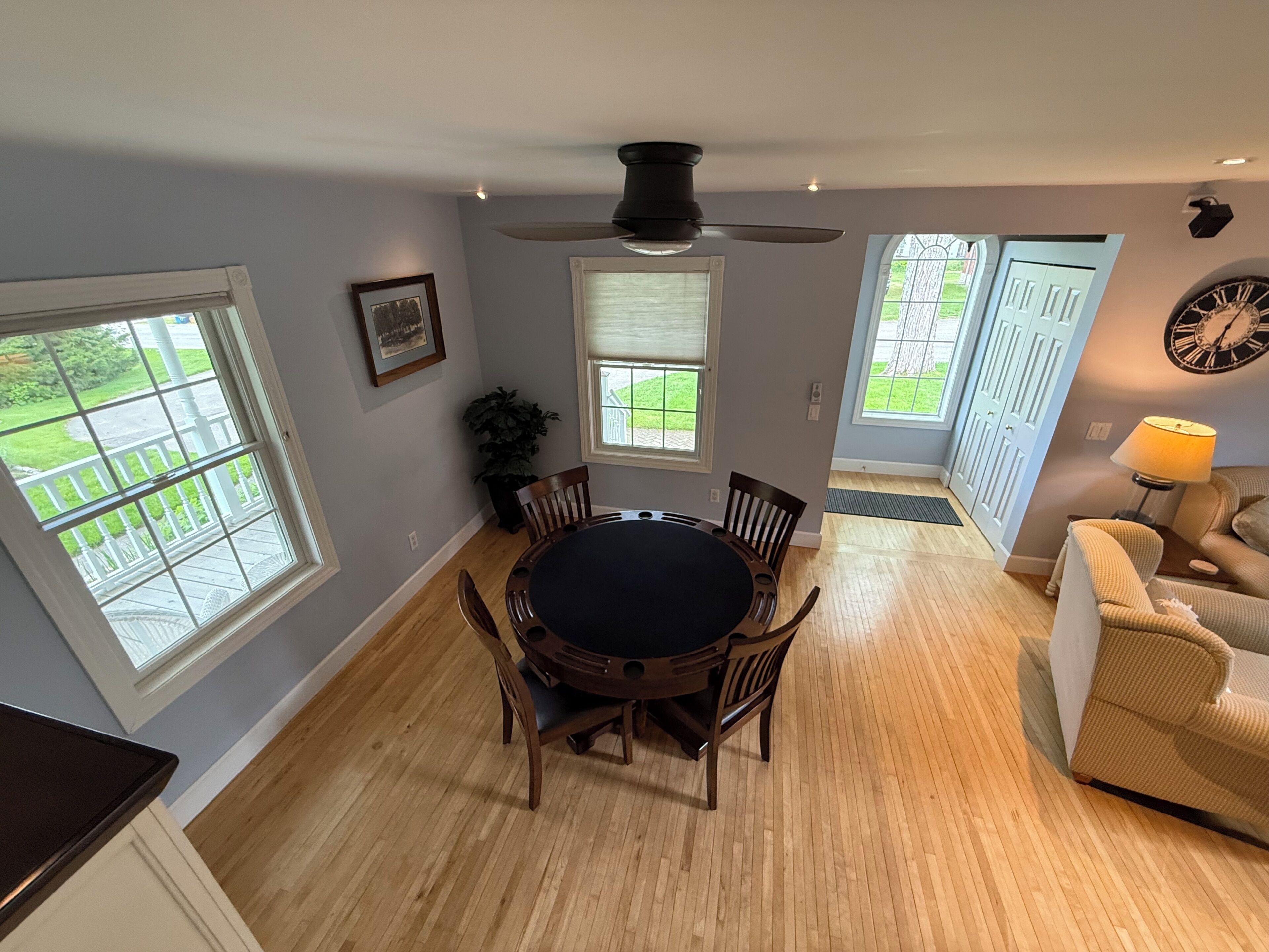 A dining area with a round table and chairs, a ceiling fan, and a view of the outdoors through large windows.
