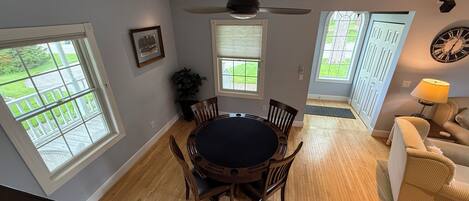 A dining area with a round table and chairs, a ceiling fan, and a view of the outdoors through large windows.