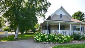 Une maison à deux étages avec un porche, entourée d’un jardin bien entretenu où poussent des hortensias.