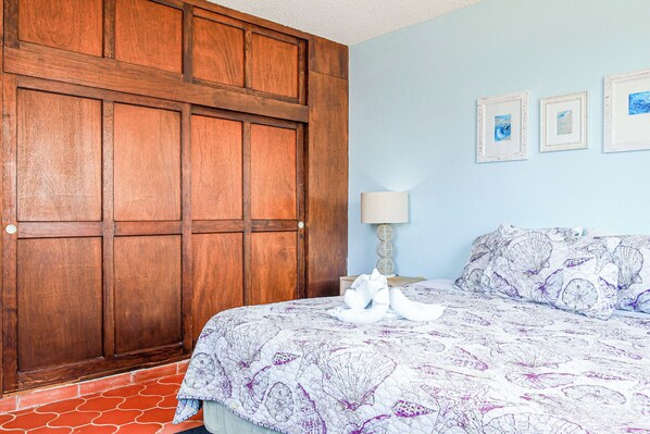 A bedroom with a wooden wardrobe, a bed with a floral-patterned bedspread, and three framed pictures on the wall. - Las Mareas 21 – Ocean View, Las Conchas (Puerto Peñasco Centro)