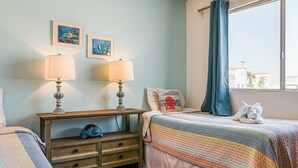 A bedroom with two beds, a nightstand with lamps, and artwork on the wall.