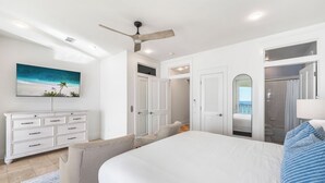 A bedroom with a large bed, a ceiling fan, a dresser, and a painting of a beach scene. - Frangista Tide*All New Furnishings*Pool*BeachSvc+Gear (Miramar Beach)