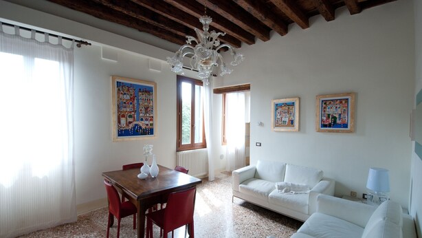Ein Wohnzimmer mit einem weißen Sofa, einem Holzespeisetisch mit roten Stühlen, einer Kristallleuchtre und zwei gerahmten Kunstwerken an der Wand.