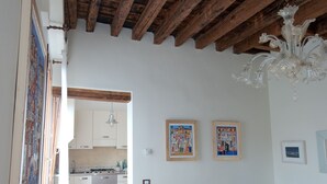 Ein Essbereich mit Holztisch, weißen Vasen und einer Chandelierleuchtre. Ein weißes Sofa und eine Küche sind im Hintergrund zu sehen.