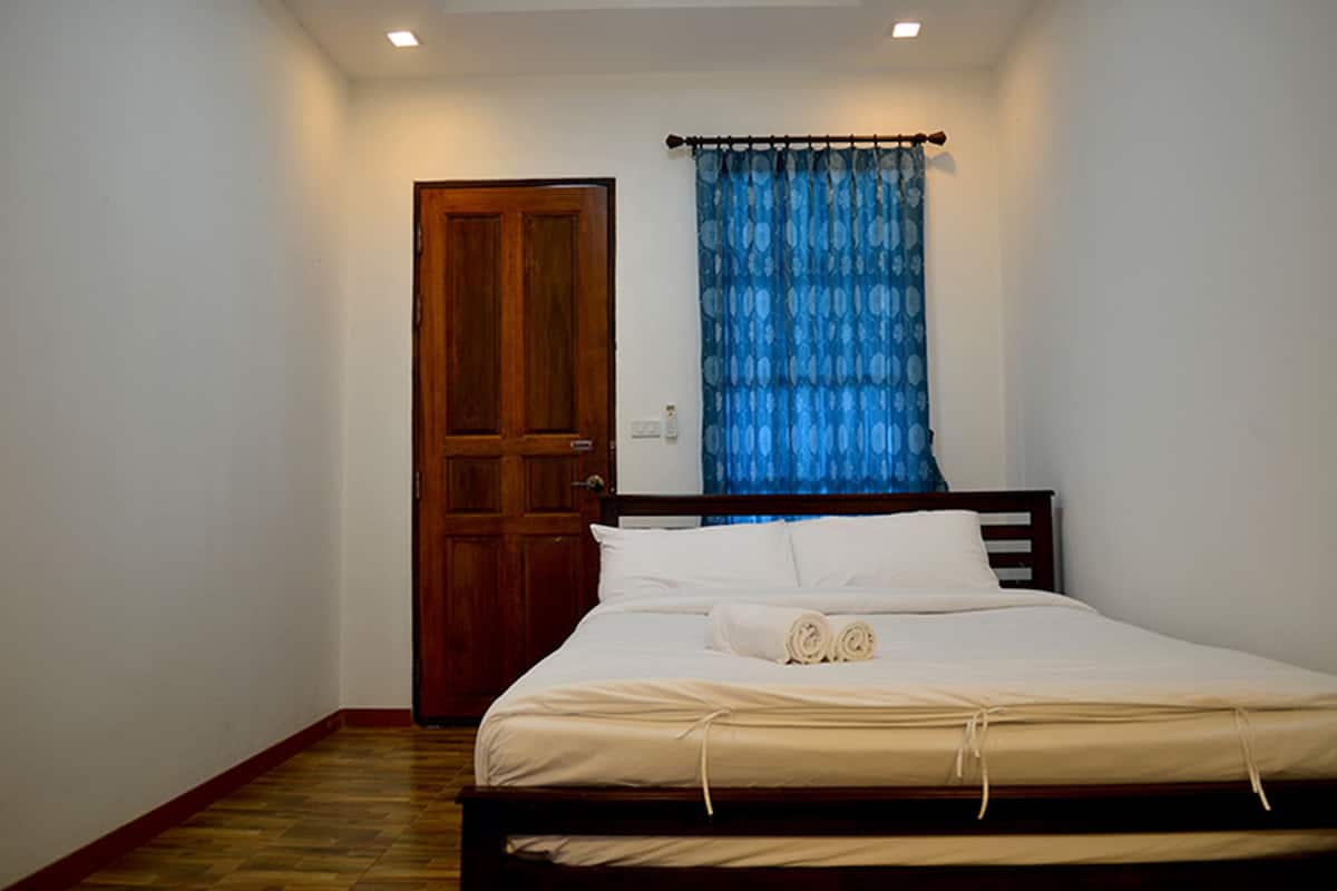 Een slaapkamer met een houten deur, een bed met wit beddengoed en een blauw gordijn.
