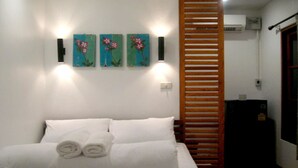 Une chambre à coucher avec un lit, des oreillers blancs et des serviettes enroulées. On y trouve trois lampes fixées au mur et une cloison en lattes de bois.