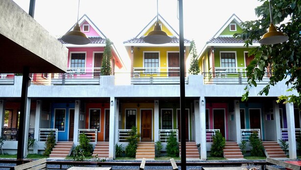 Una hilera de casas coloridas con balcones, un espacio de estar al aire libre cubierto con mesas y bancos, y una vista despejada del cielo.