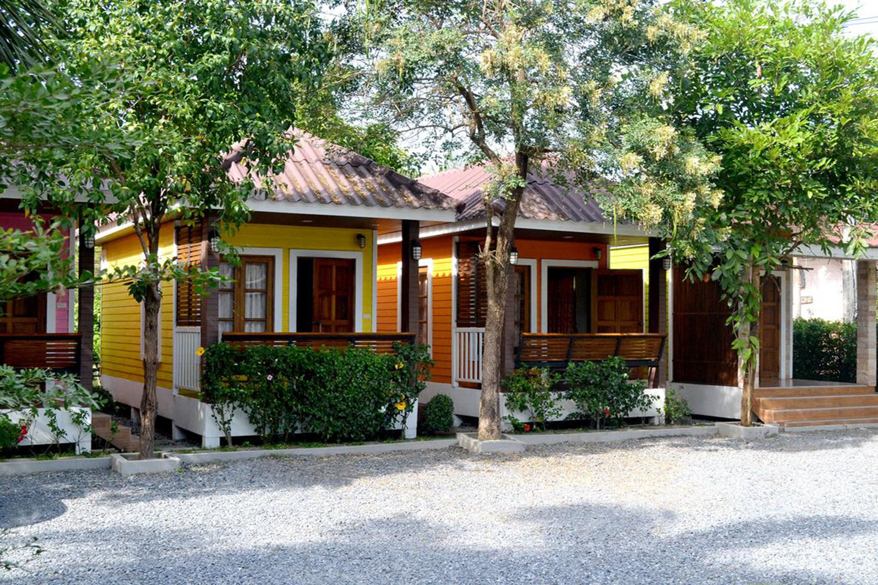 A row of yellow and orange cabins with wooden balconies, surrounded by greenery and gravel paths.