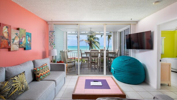 A living room with a grey sofa, colorful cushions, a teal bean bag, and a flat-screen TV. - 205E La Brisa-2BR 2BA beachfront condo w/parking, shared pool, grills (Key West)