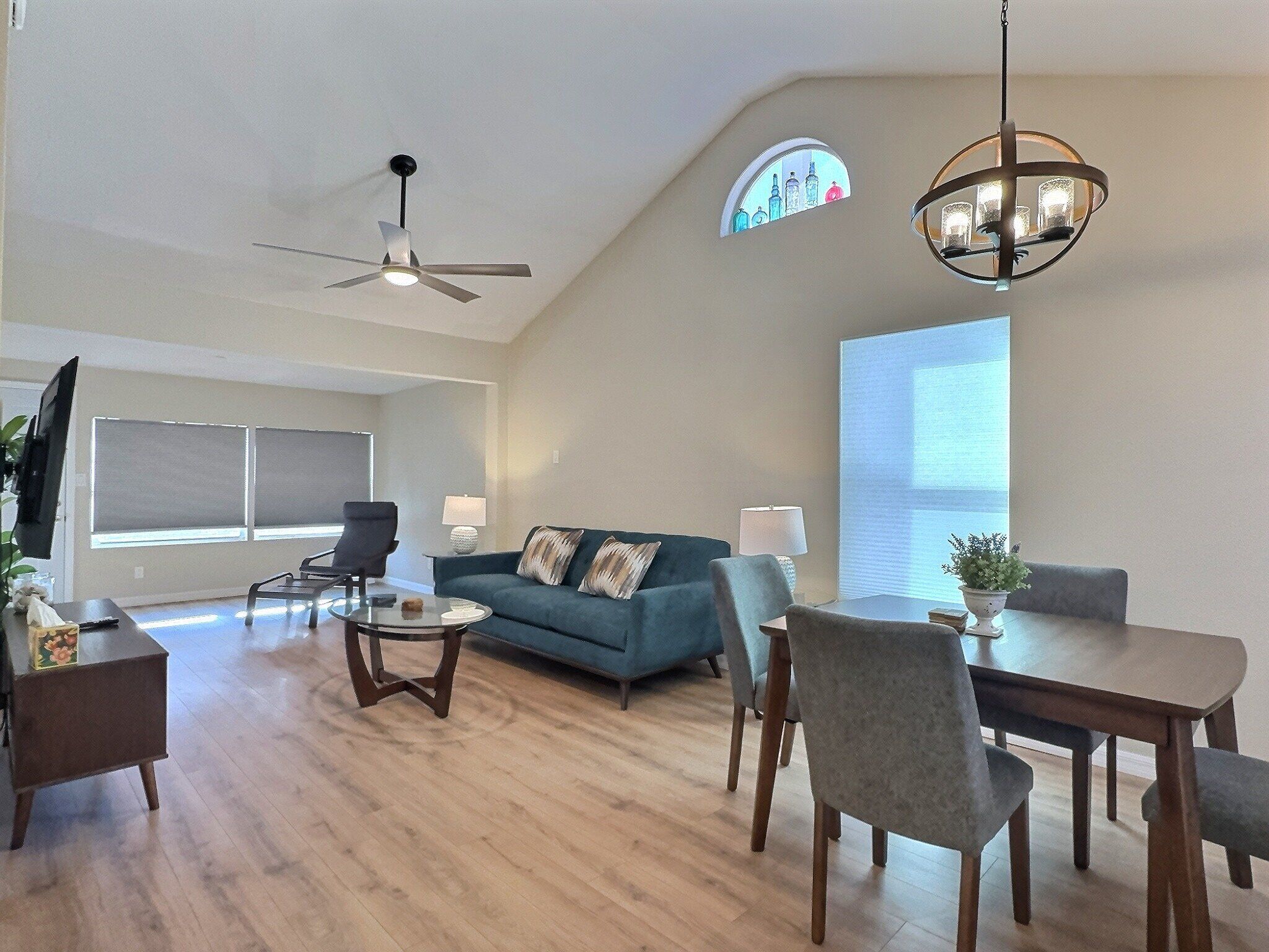 A spacious living room with a ceiling fan, a dining area with a table and chairs, a blue sofa, and a chandelier.