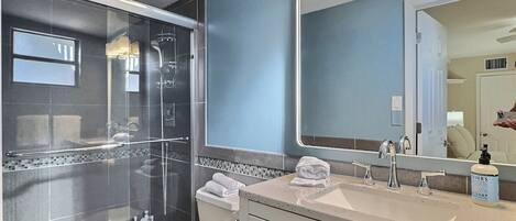 Une salle de bain moderne avec une douche en verre, un grand miroir et un meuble-lavabo avec un évier et des articles de toilette.