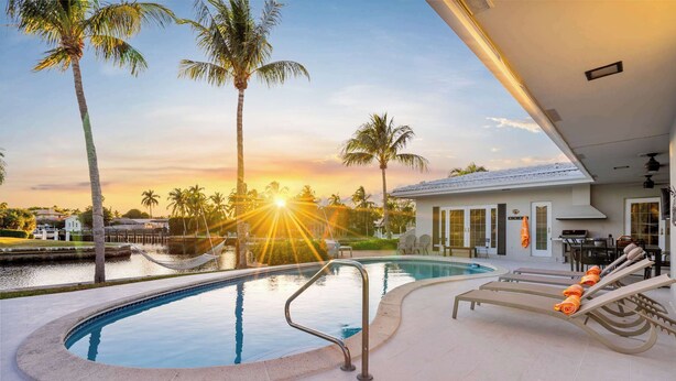 A swimming pool with lounge chairs and a view of the sunset. - 5 Bedroom Private Waterfront Villa with Pool and Dock (Fort Lauderdale)