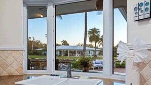 A kitchen with a double sink, granite countertop, and large windows offering a view of a pool and palm trees. - 5 Bedroom Private Waterfront Villa with Pool and Dock (Fort Lauderdale)