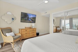 Une chambre avec un grand lit, une télévision, un fauteuil en osier, une commode et une vue sur l’extérieur.