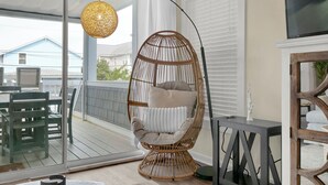 A wicker chair with cushions, a round woven light fixture, and a view of a house through a glass door. - Relaxing townhouse with beautiful ocean views and just steps to the beach! (Wrightsville Beach)