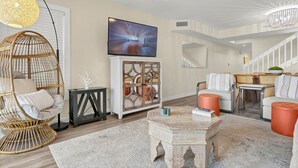 A living room with a television, wicker chair, white sofa, and a staircase. - Relaxing townhouse with beautiful ocean views and just steps to the beach! (Wrightsville Beach)