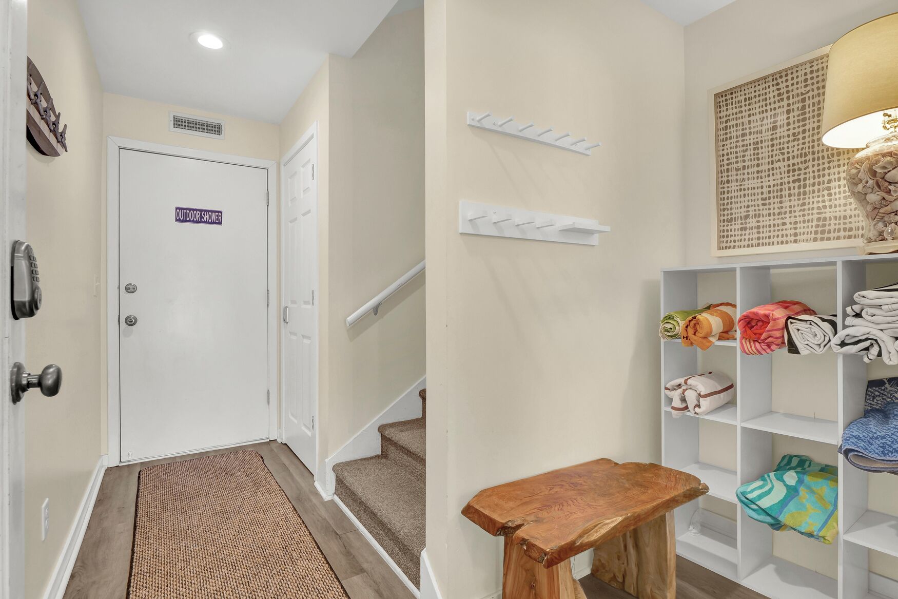 Un pasillo con una puerta que indica 'DUCHA EXTERIOR', un banco de madera, una escalera y un estante con ropa doblada.