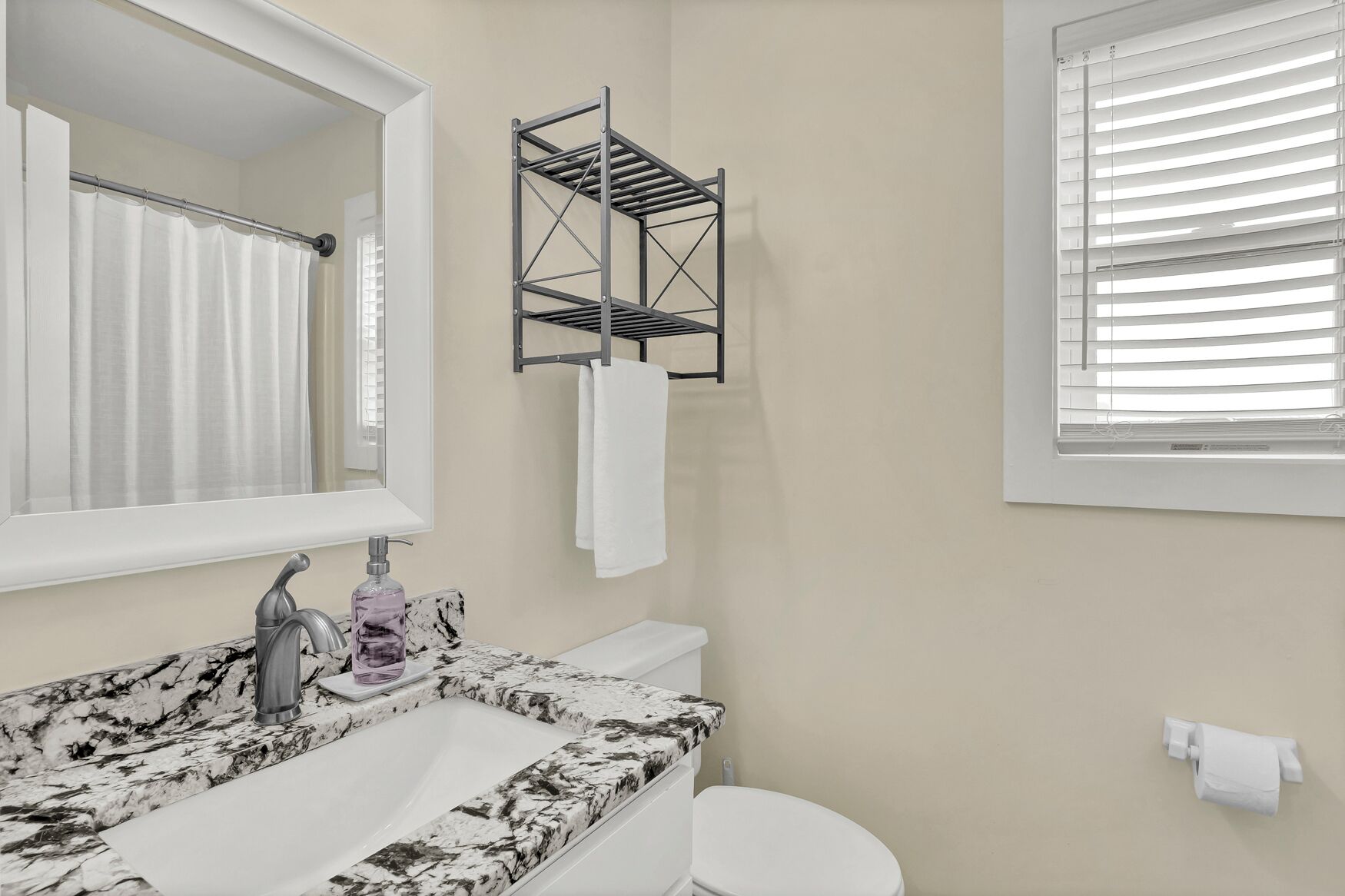 A bathroom with a marble sink, a toilet, a towel rack, and a window with blinds.