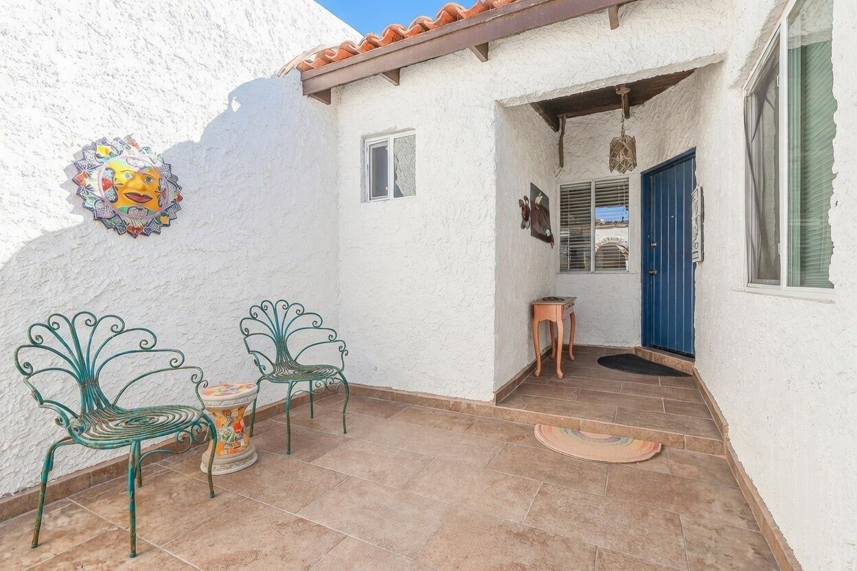 Un patio con dos sillas de metal verde, una mesa pequeña y un adorno de pared.