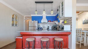 Une cuisine avec un îlot central rouge, trois tabourets, un réfrigérateur blanc, un four à micro-ondes et une cuisinière.