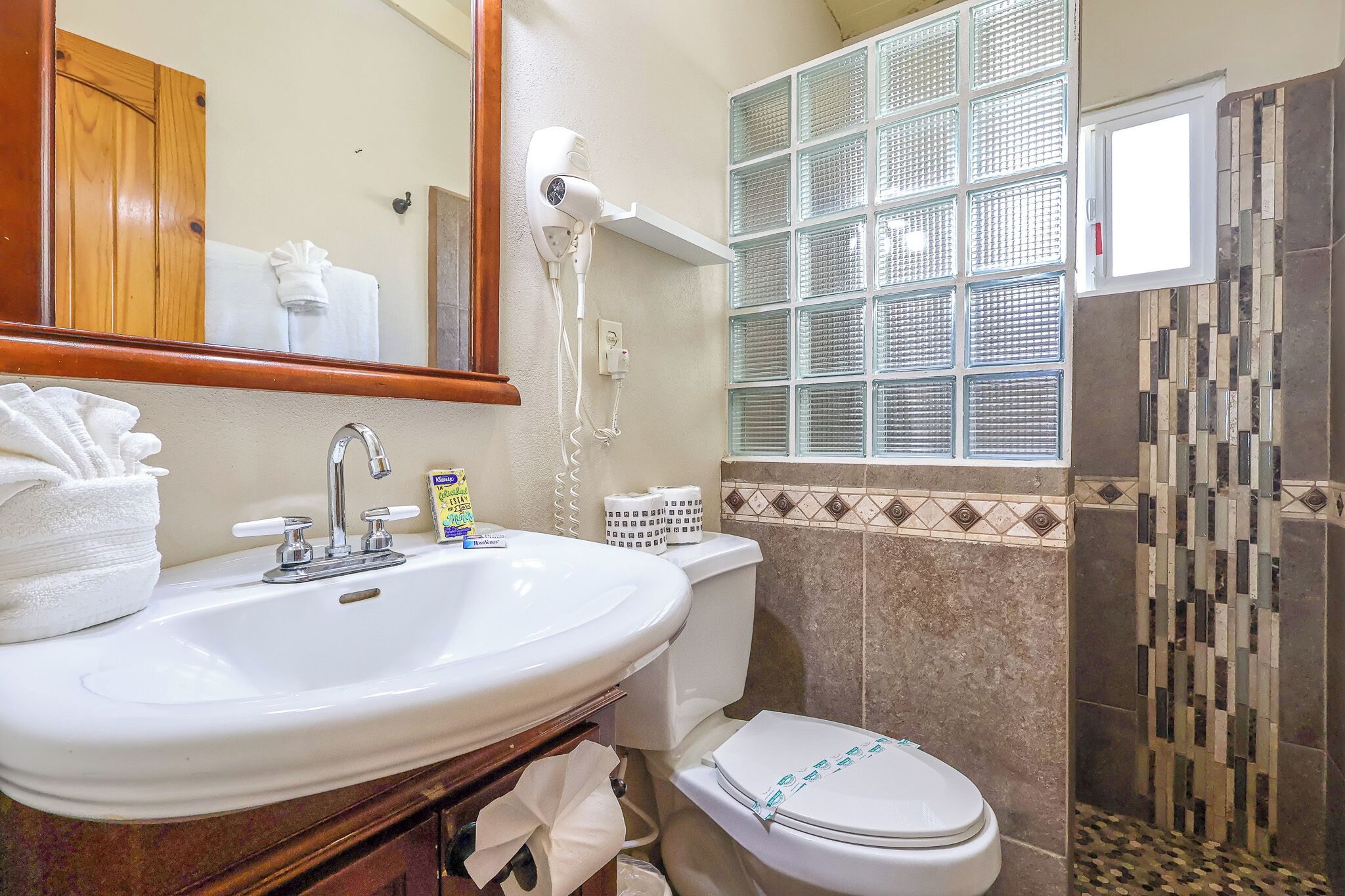 A bathroom with a sink, mirror, towel, toilet, and a shower area.