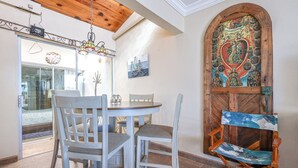 Un coin repas comprenant une table ronde et quatre chaises, un plafond en bois et une porte décorative ornée d’un tableau.