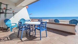 Une terrasse avec des chaises bleues et une table, d’où l’on a une vue sur la mer.