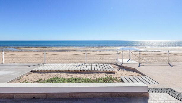 Une vue sur la plage avec une terrasse en bois et une barrière en chaîne.