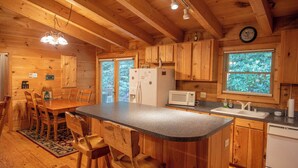 A wooden cabin interior with a kitchen featuring a central island, wooden cabinets, a refrigerator, a microwave, and a sink. - Nature Hideout with Great Location | Bear's Den Log Cabin | Hot Tub & Two Decks (Fleetwood)