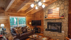 A cozy cabin interior with a stone fireplace, leather sofa, and a television. - Nature Hideout with Great Location | Bear's Den Log Cabin | Hot Tub & Two Decks (Fleetwood)