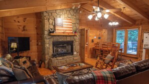 A cozy cabin interior with a stone fireplace, leather furniture, and a television. - Nature Hideout with Great Location | Bear's Den Log Cabin | Hot Tub & Two Decks (Fleetwood)