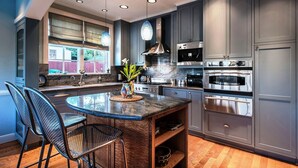 A modern kitchen with a central island, stainless steel appliances, and a window overlooking a backyard. - 3684 Jewel by the Sea ~ Walk to Town and the Beach (Pacific Grove)