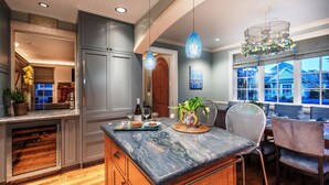 A modern kitchen with a marble countertop, wooden cabinets, and a dining area with a view of the outside. - 3684 Jewel by the Sea ~ Walk to Town and the Beach (Pacific Grove)