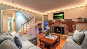A living room with a fireplace, a television mounted above it, and a staircase leading to another level. - 3684 Jewel by the Sea ~ Walk to Town and the Beach (Pacific Grove)