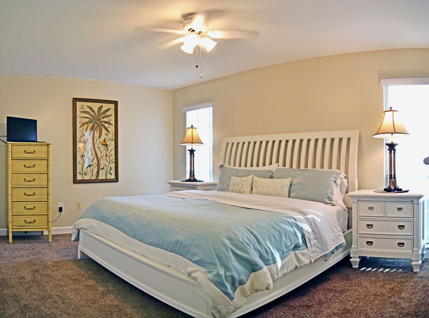 A bedroom with a bed, two bedside tables, a ceiling fan, a window, and a painting on the wall.