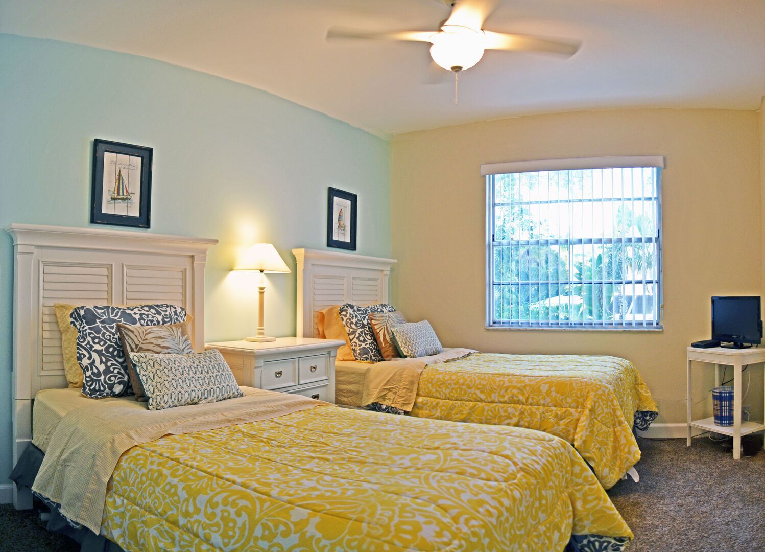 A bedroom with two beds, a ceiling fan, a window with bars, and a television on a small table.