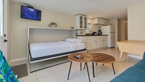 A compact room with a bed, a small table, a TV, a kitchenette, and a bathroom. - Beachside Studio Located Across from Main Beach and Half Mile to Village (Sarasota)