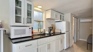A modern kitchen with white cabinetry, a black countertop, and a built-in microwave. - Beachside Studio Located Across from Main Beach and Half Mile to Village (Sarasota)