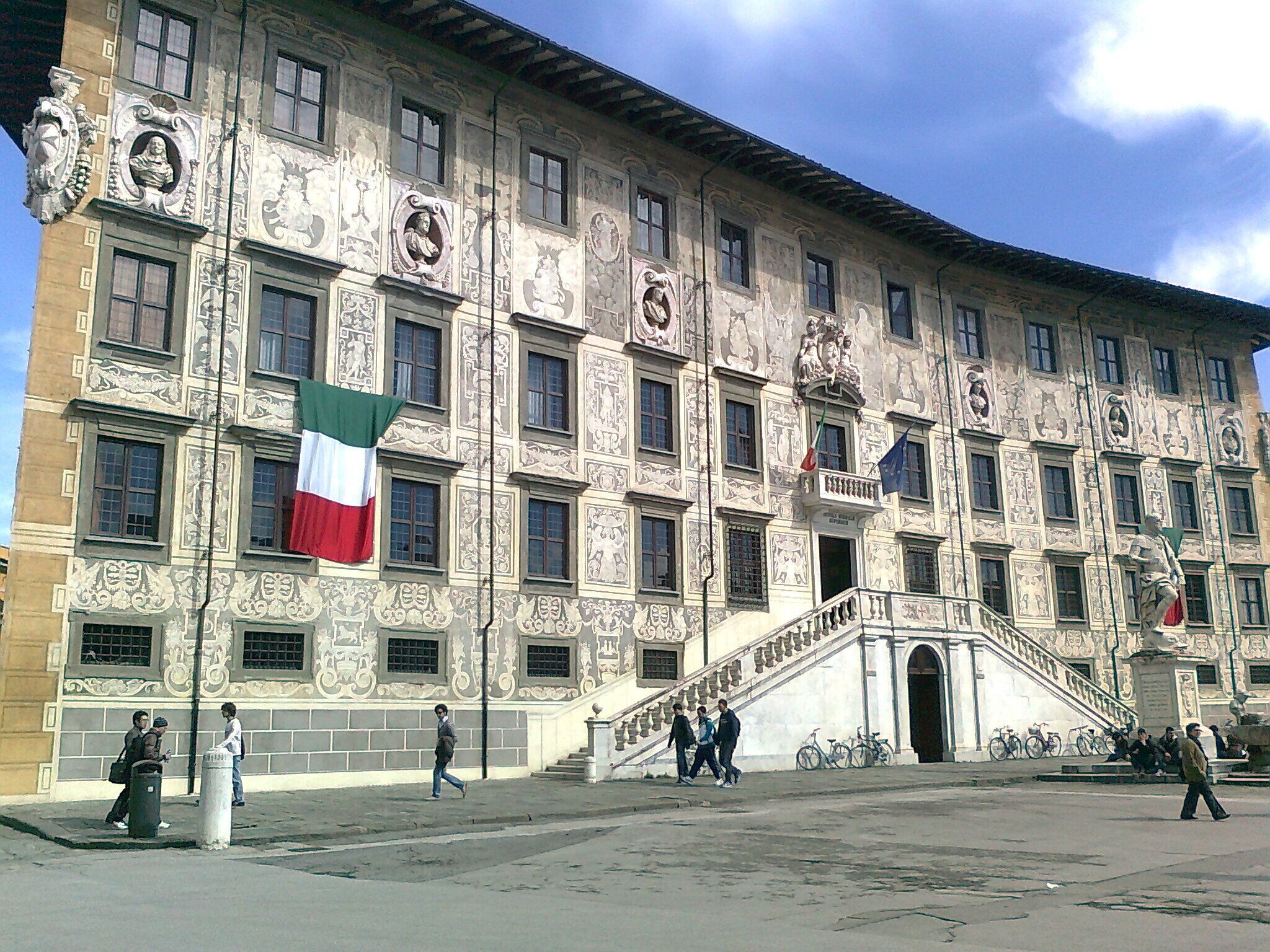 A historic building with ornate facades, multiple flags, and a central staircase leading to an entrance.
